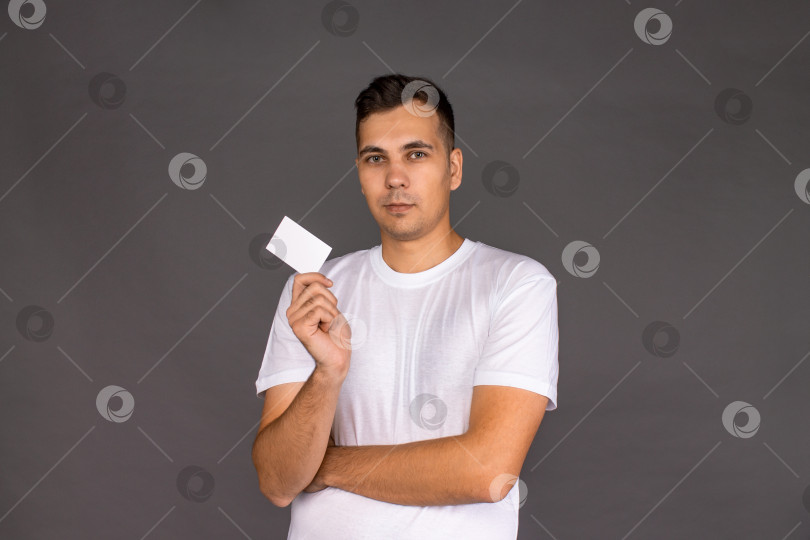 Скачать Молодой человек в белой футболке держит в руках визитную карточку фотосток Ozero