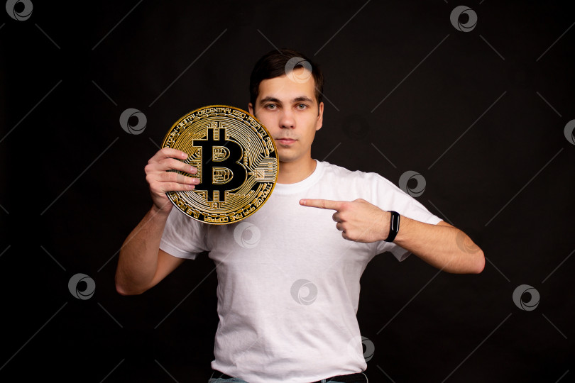 Скачать Молодой парень держит в руках символ монеты Биткоин, современной валюты для обмена и покупок фотосток Ozero