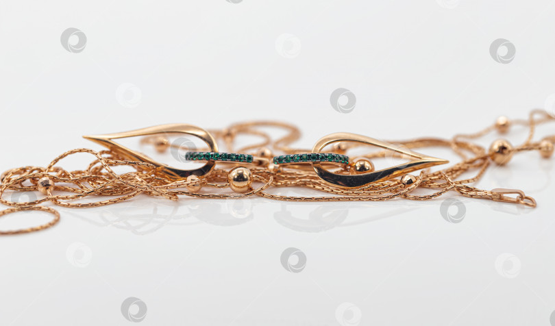 Скачать Элегантные золотые серьги в форме капли с изумрудами окружены тонким золотым ожерельем фотосток Ozero