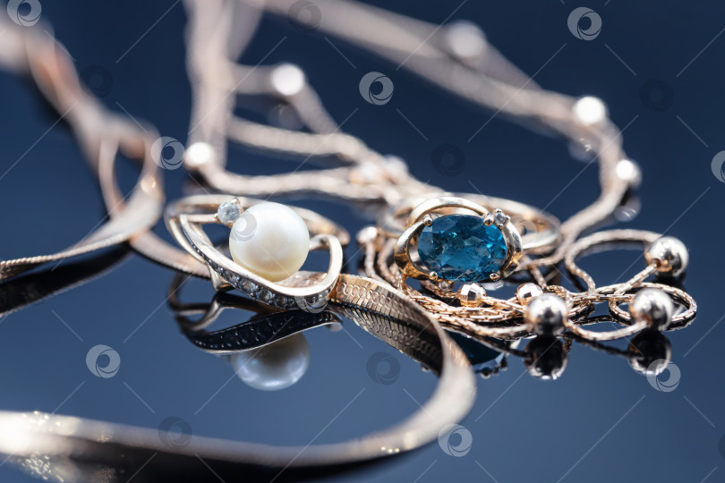 Скачать Золотые кольца с разными драгоценными камнями лежат в окружении красивых золотых цепочек фотосток Ozero