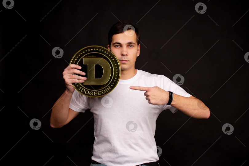 Скачать Молодой парень держит в руках символ монеты dogecoin, современной валюты для обмена и покупок фотосток Ozero