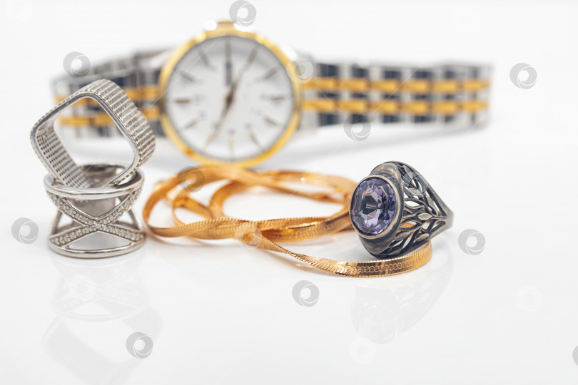 Скачать Серебряные кольца разной формы и золотая цепочка лежат на фоне женских наручных часов фотосток Ozero