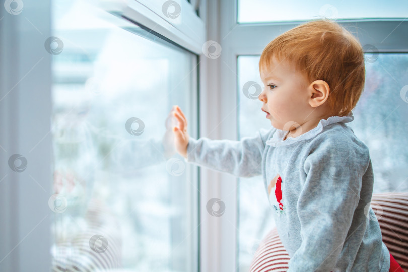 Скачать малыш внимательно смотрит в окно на снег и на то, что происходит вокруг, вид сбоку, крупный план с пробелом для текста фотосток Ozero