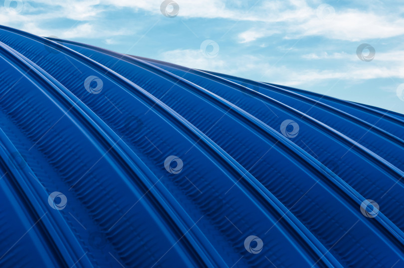 Скачать Крыша ангара из синего металлопроката на фоне неба с облаками. Металлическая конструкция промышленного здания снаружи. Современные архитектурные технологии фотосток Ozero