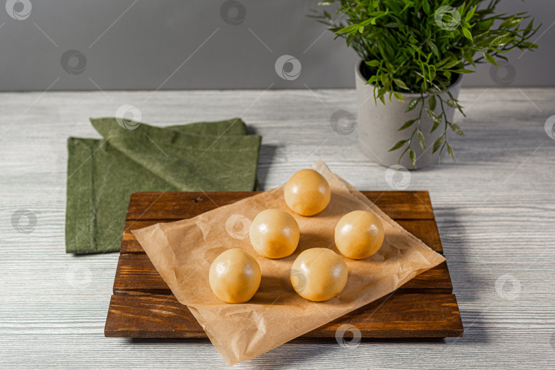 Скачать пять шариков из теста для печенья разложите на бумаге для выпечки и на кухонном деревянном столе, застеленном зеленой салфеткой фотосток Ozero