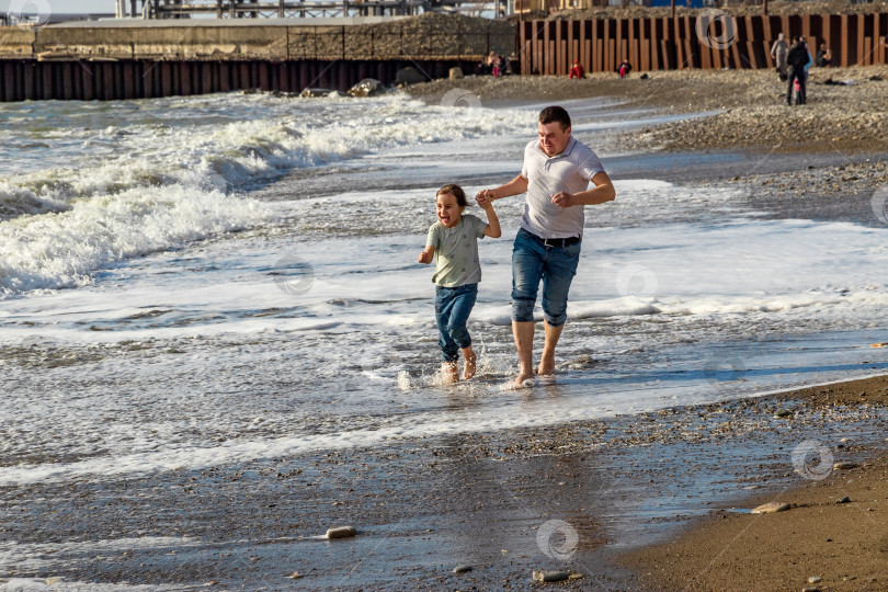 Скачать Отец и дочь убегают от набегающих волн. фотосток Ozero