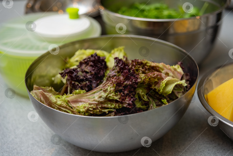 Скачать Крупный план промытых листьев свежего салата в миске из нержавеющей стали на кухонном столе фотосток Ozero