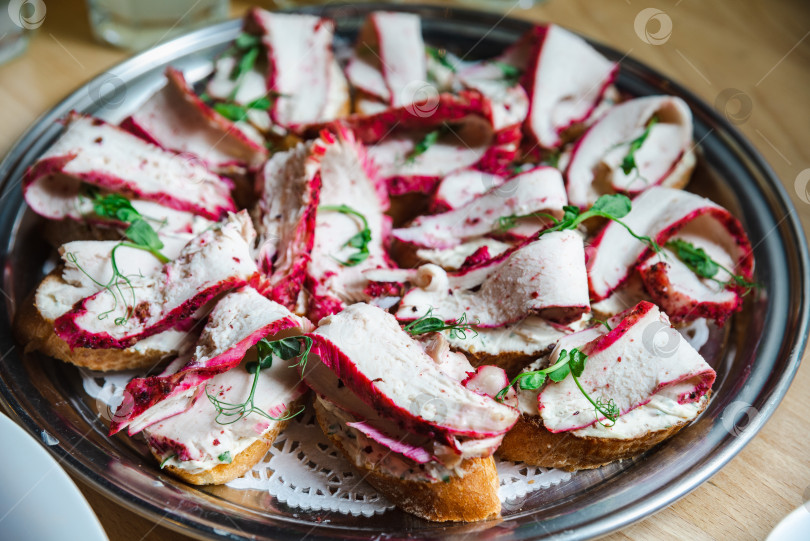 Скачать брускетта с мясом птицы, подрумяненная свеклой и украшенная зеленым горошком на тарелке. фотосток Ozero