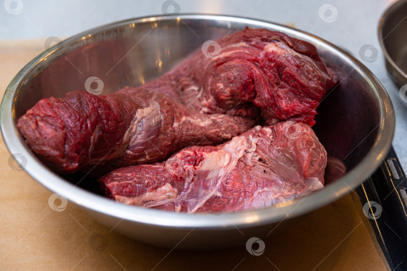 Скачать Сырое говяжье мясо в металлической миске на кухонной столешнице. Нежная говядина готова к приготовлению. фотосток Ozero