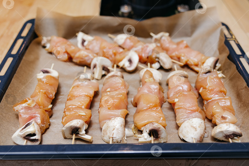 Скачать Крупный план шашлыков из сырой курицы с шампиньонами на деревянных шпажках на бумаге для выпечки на противне для духовки, маринованная птица фотосток Ozero