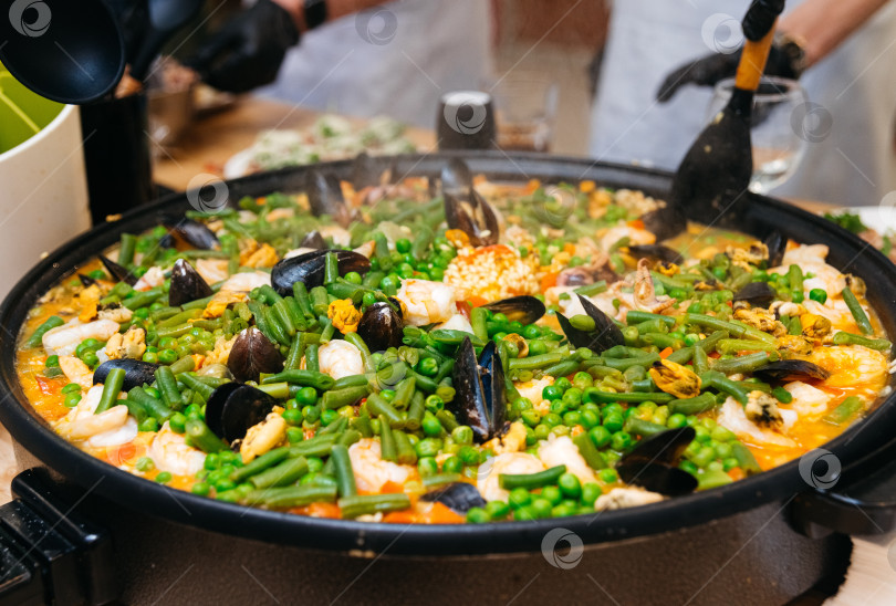 Скачать приготовление паэльи с морепродуктами и овощами на кулинарном мастер-классе. большая сковорода для паэльи готовится на пару. фотосток Ozero