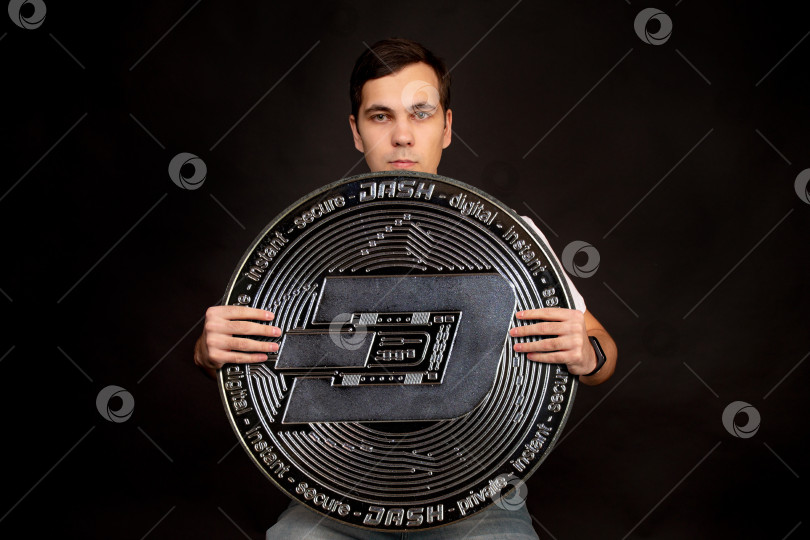 Скачать Молодой парень держит в руках символ монеты DASH, современной валюты для обмена и покупок фотосток Ozero