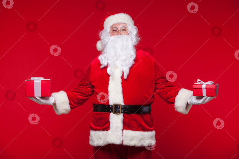 Скачать Рождество. Фотография Санта-Клауса, дающего рождественский подарок и смотрящего в камеру, на красном фоне фотосток Ozero