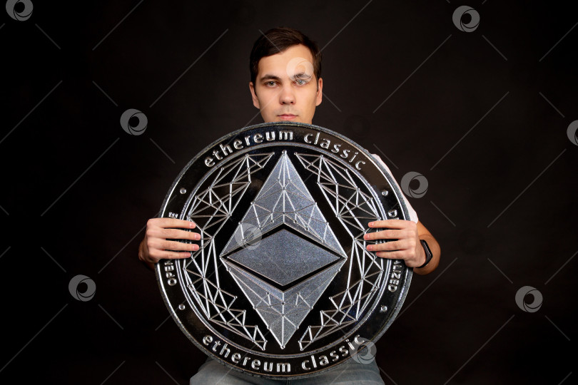 Скачать На заднем плане стоит мужчина с монетой в руках ethereum classic. фотосток Ozero