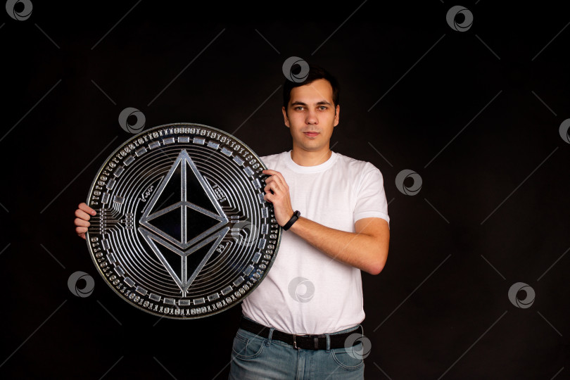 Скачать На заднем плане стоит мужчина с монетой в руках ethereum classic. фотосток Ozero