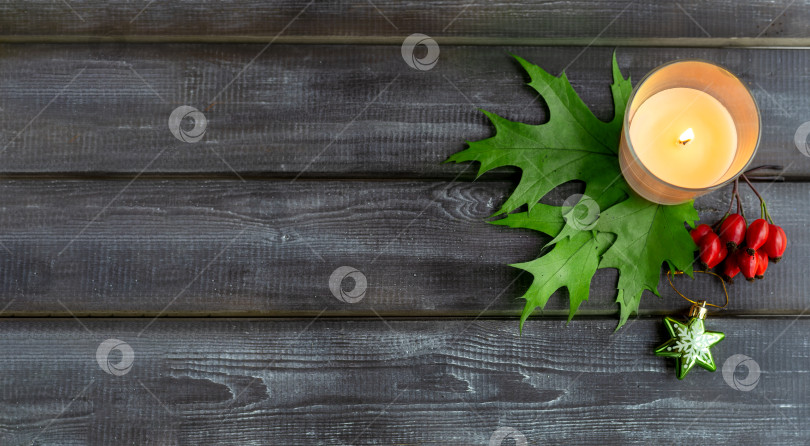 Скачать Деревянный рождественский фон, украшенный зелеными листьями остролиста, красными ягодами и горящей свечой. Вид сверху. Пространство для копирования фотосток Ozero