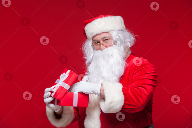 Скачать Рождество. Фотография Санта-Клауса, дающего рождественский подарок и смотрящего в камеру, на красном фоне фотосток Ozero