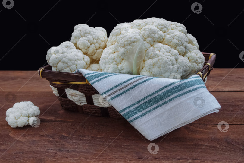 Скачать Кочан белой цветной капусты в плетеной корзине на коричневом деревянном столе на темном фоне фотосток Ozero