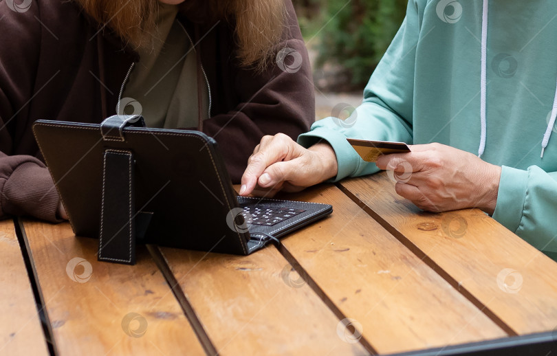 Скачать Счастливая зрелая бабушка с внучкой, использующей кредитную карту, делают покупки онлайн на ноутбуке. фотосток Ozero