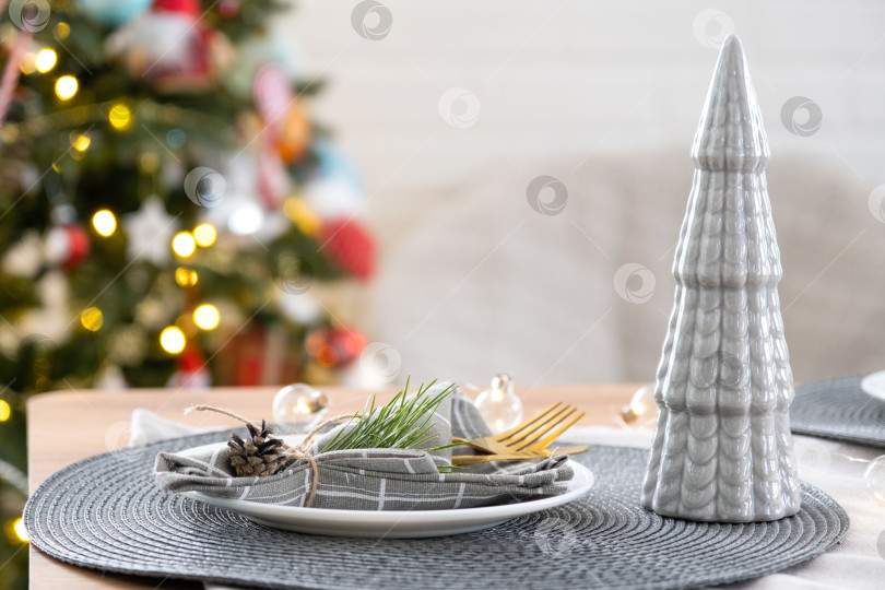 Скачать Сервировка праздничного стола тарелками, вилками, ножами, салфетками крупным планом из ткани в клетку, украшенная к Рождеству и Новому году сосновой веткой с шишкой. Эко-стиль, минимализм фотосток Ozero