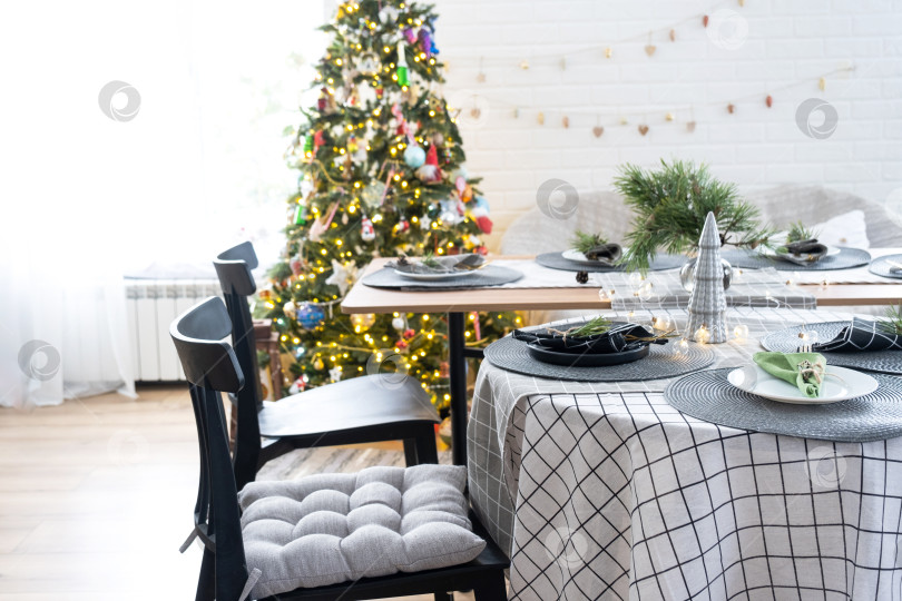 Скачать Сервировка праздничного стола тарелками, вилками, ножами, салфетками, бокалами крупным планом в современном интерьере лофт-дома, украшенного к Рождеству и Новому году. Ждем гостей на праздничный ужин фотосток Ozero