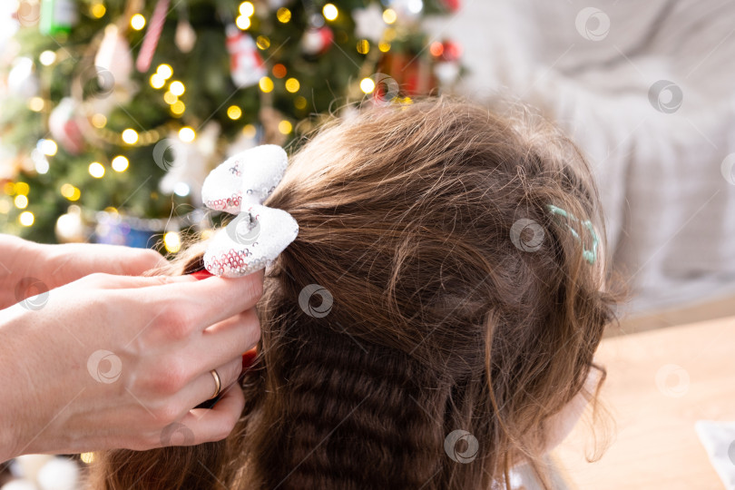 Скачать Длинные волосы девочки с блестящим бантом - мамины руки расчесывают дочку к празднику на фоне огней рождественской елки дома фотосток Ozero
