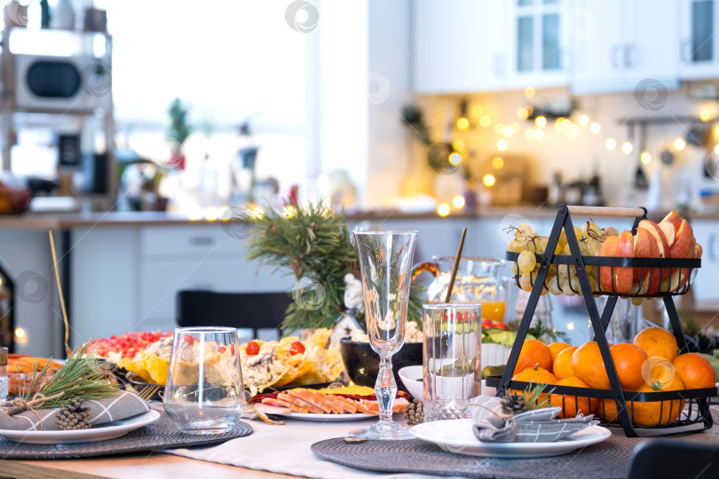 Скачать Сервировка праздничного стола с закусками, салатами и вкусностями крупным планом в современном интерьере лофт-дома, украшенного к Рождеству и Новому году. Ждем гостей на праздничный ужин фотосток Ozero