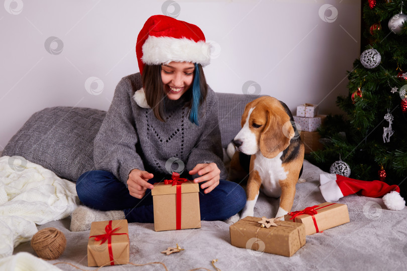 Скачать Девочка в шапке Санта-Клауса открывает подарочную коробку. фотосток Ozero