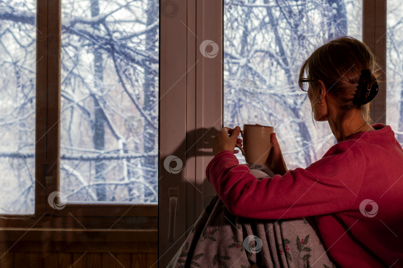 Скачать женщина пьет кофе ранним зимним утром и любуется заснеженными деревьями за своим окном. Хюгге, уютный фотосток Ozero