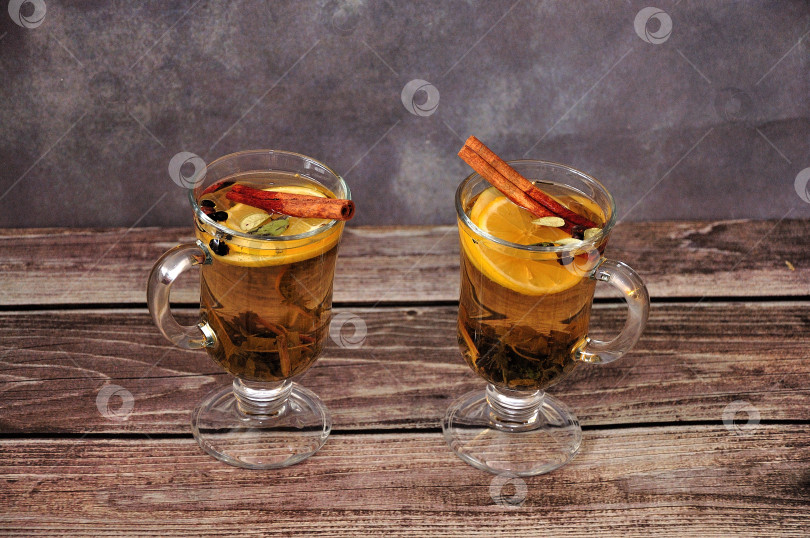 Скачать Два стеклянных стакана травяного чая со специями, ломтиком лимона и палочками корицы на деревянном столе. фотосток Ozero