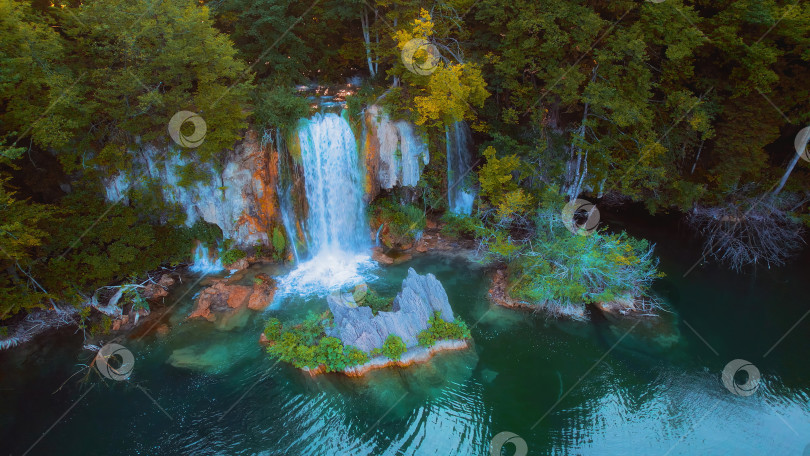 Скачать Живописный мощный водопад течет в зеленом лесу. Чистая пресная вода озера. Природа сумеречного заката. фотосток Ozero