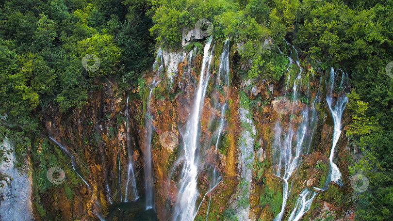 Скачать Горный водопад стекает с высокой скалы в национальном парке. Чистая вода со множеством ручьев. Плитвице, Хорватия. фотосток Ozero