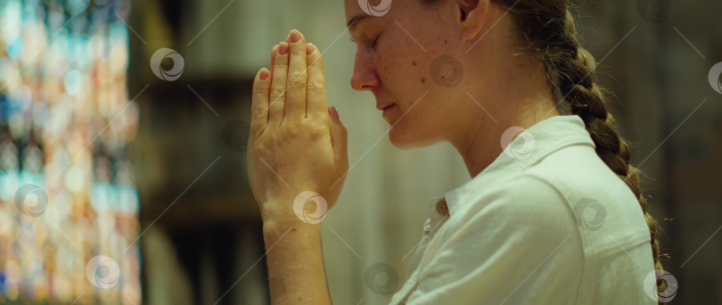 Скачать Женщина молится в церкви. Искренне верующая взрослая девушка поклоняется Богу в кафедральном соборе. фотосток Ozero