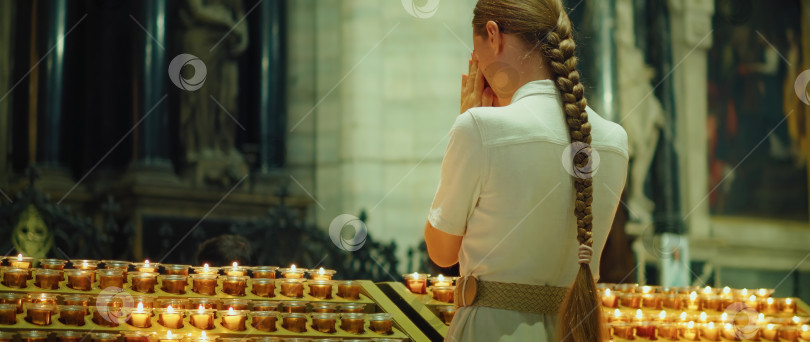 Скачать Женщина молится в кафедральном соборе. Религиозная взрослая девушка в длинном платье с аккуратно уложенными волосами, заплетенными в тугую косу. фотосток Ozero