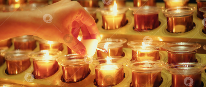 Скачать Крупный план женской руки, держащей свечу и зажигающей ее от другой горящей свечи в церкви. фотосток Ozero