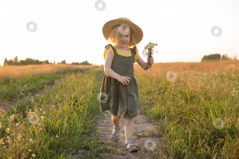Скачать Маленькая светловолосая девочка в соломенной шляпке прогуливается по полю с букетом ромашек. Концепция прогулок на природе, свободы и экологически чистого образа жизни. фотосток Ozero