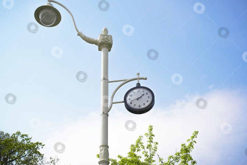Скачать Часы на старинном ретро-столбе в парке. Циферблат на фоне голубого неба в солнечный день. Уличные часы фотосток Ozero