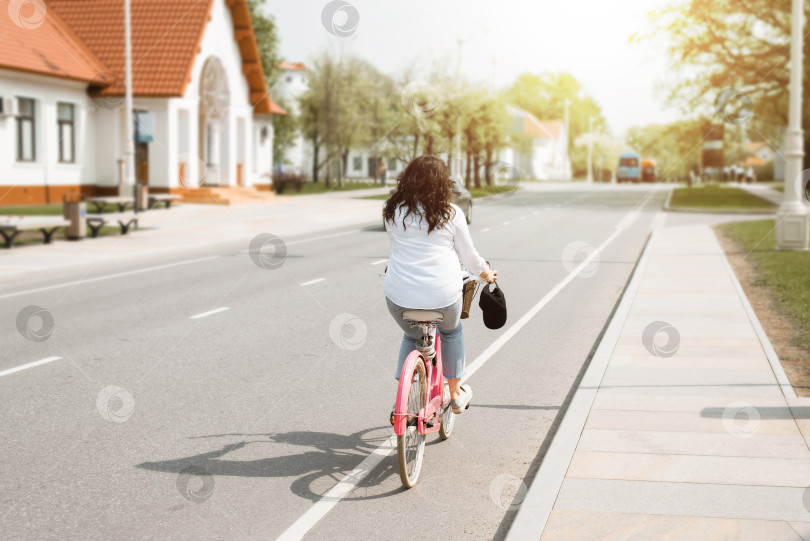 Скачать Женщина едет на велосипеде солнечным летним днем. Активная езда на розовом велосипеде по улице. Велосипедист, вид сзади, неузнаваемая личность. фотосток Ozero