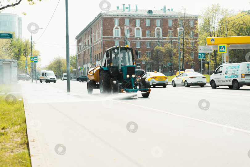 Скачать Влажная уборка городских улиц. Специальная техника поливает тротуар и чистит асфальт в городе в течение дня. Москва, Россия 05.12.2021 фотосток Ozero