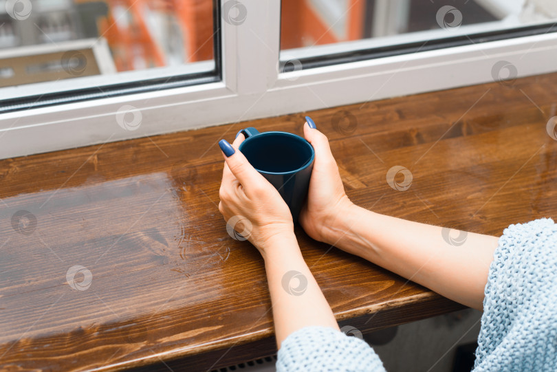 Скачать Женщина пьет кофе в помещении. Крупным планом женские руки, держащие чашку кофе на подоконнике у окна. Обрезанное изображение. фотосток Ozero