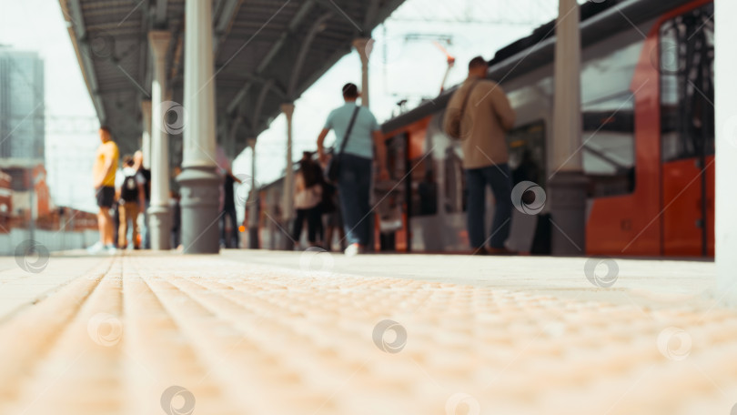 Скачать Расфокусированные пассажиры на железнодорожном вокзале в ожидании поезда. Вид под низким углом на неузнаваемый размытый поезд и людей, стоящих и прогуливающихся по платформе солнечным летним днем на открытом воздухе фотосток Ozero