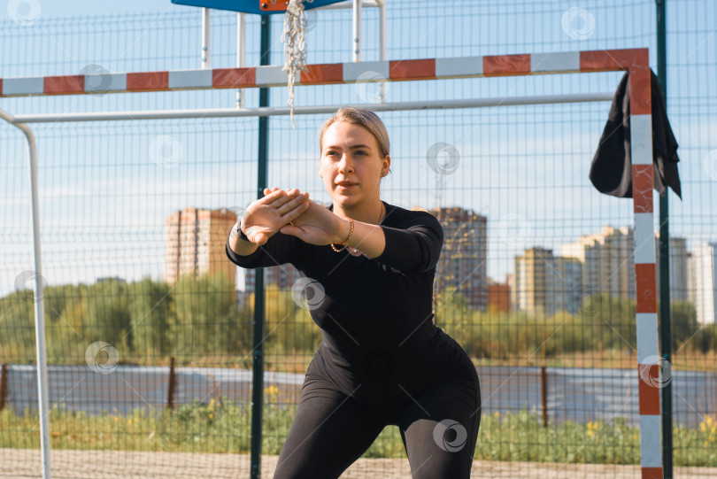 Скачать Тренировка на спортивной площадке, на свежем воздухе. Красивая молодая женщина в обтягивающей спортивной одежде тренируется на открытом воздухе. Спортсмен по фитнесу делает приседания. Здоровый образ жизни фотосток Ozero