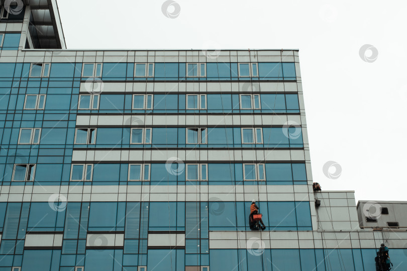 Скачать Рабочий, моющий окна высотного здания, снаружи. Промышленные альпинисты фотосток Ozero