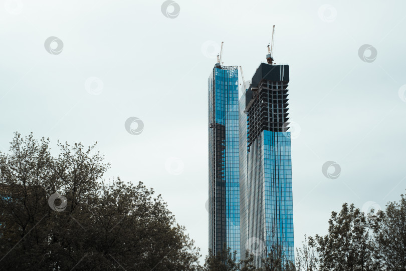 Скачать Строящиеся небоскребы, внешний вид. Краны на крышах современных высотных зданий, завершающие их фотосток Ozero
