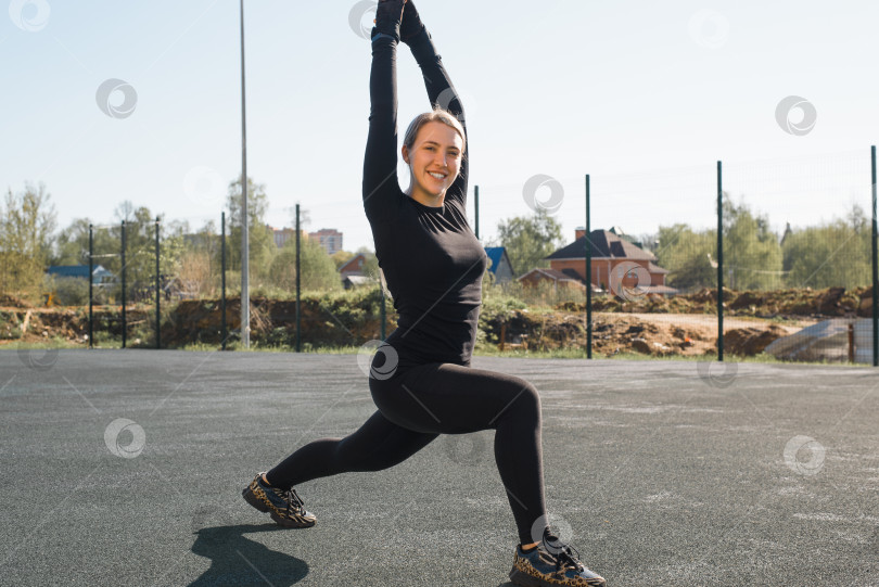 Скачать Спортсменка потягивается на спортивной площадке. Улыбающаяся молодая блондинка занимается фитнесом по утрам. Портрет счастливой спортсменки, тренирующейся. Спортивная тренировка на открытом воздухе. Здоровый активный образ жизни фотосток Ozero