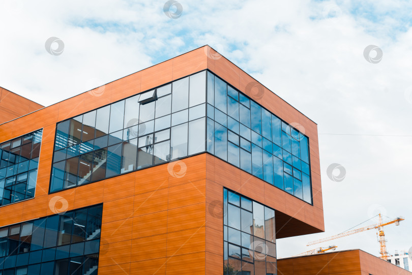 Скачать Внешний вид офисного здания. Современная минималистская городская архитектура снаружи. Здание имеет форму квадрата с деревянными панелями и синими окнами. фотосток Ozero