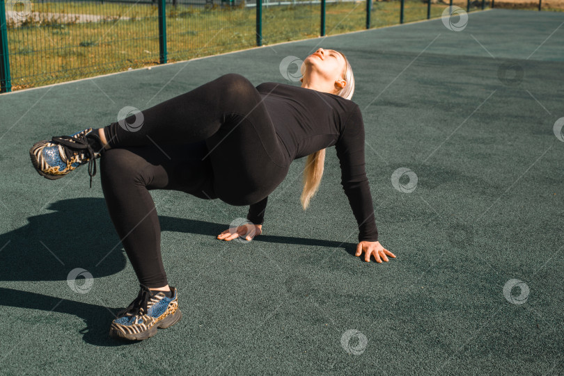 Скачать Спортсменка в черном облегающем спортивном костюме потягивается на детской площадке. Фитнес-молодая женщина занимается йогой по утрам. Тренированный спортсмен, занимается уличным спортом. Здоровый активный образ жизни фотосток Ozero