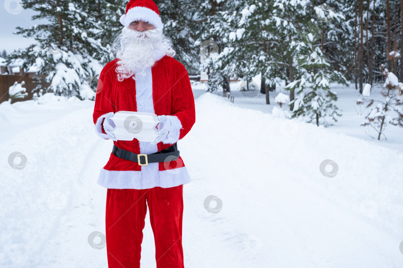 Скачать Контейнеры службы доставки еды в руках Санта-Клауса на открытом воздухе в снегу. Акция в канун Рождества. Готовый горячий заказ, одноразовая пластиковая коробка. Кейтеринг на новогодние праздники. Пространство для копирования, макет фотосток Ozero