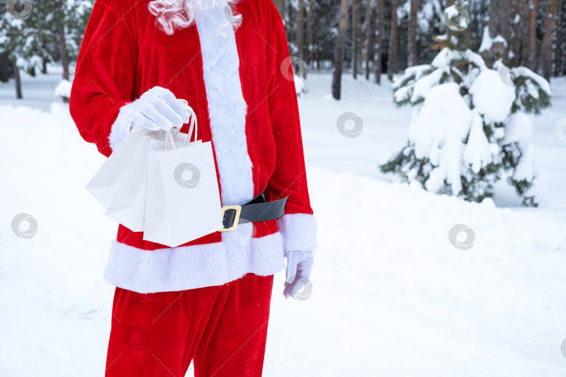 Скачать Санта-Клаус на открытом воздухе зимой и в снегу вручает в руки бумажные пакеты с подарками ручной работы, доставка еды. Покупки, переработка упаковки, ручная работа, доставка на Рождество и Новый год фотосток Ozero