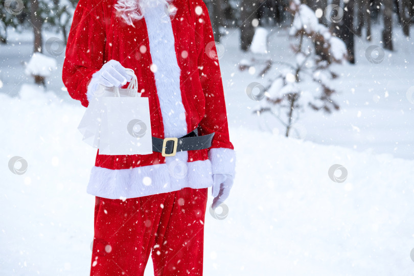 Скачать Санта-Клаус на открытом воздухе зимой и в снегу вручает в руки бумажные пакеты с подарками ручной работы, доставка еды. Покупки, переработка упаковки, ручная работа, доставка на Рождество и Новый год фотосток Ozero